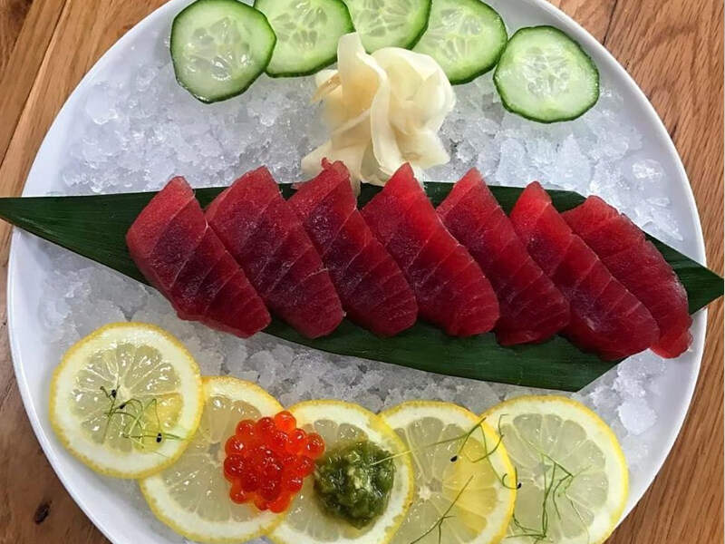 Overhead view of 7 pieces of raw tuna on a banana leave on a plate of ice