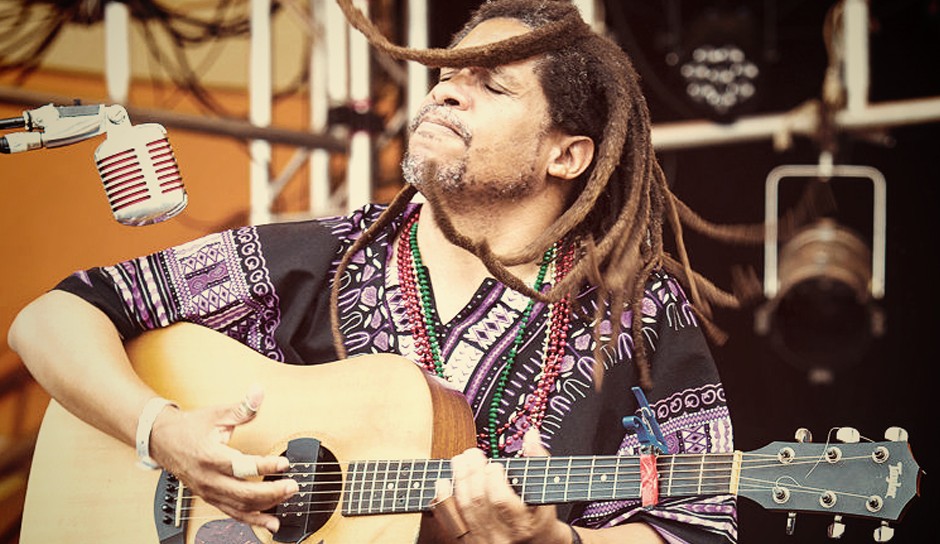 man with dreadlocks playing an acoustic guitar