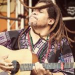 man with dreadlocks playing an acoustic guitar
