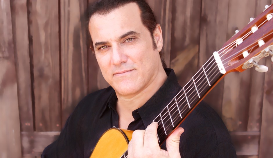 man in black shirt holding an acoustic guitar in front of a wood wall