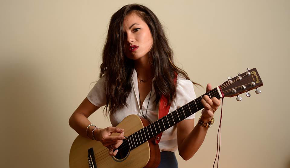 Woman with dark hair playing an acoustic guitar