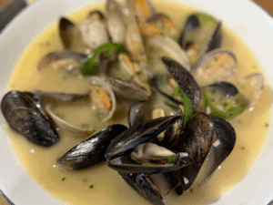 A bowl of mussels and clams in a creamy broth, garnished with chopped herbs.