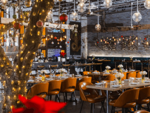 A modern restaurant with orange chairs, wooden tables, string lights, and hanging decorative globes.